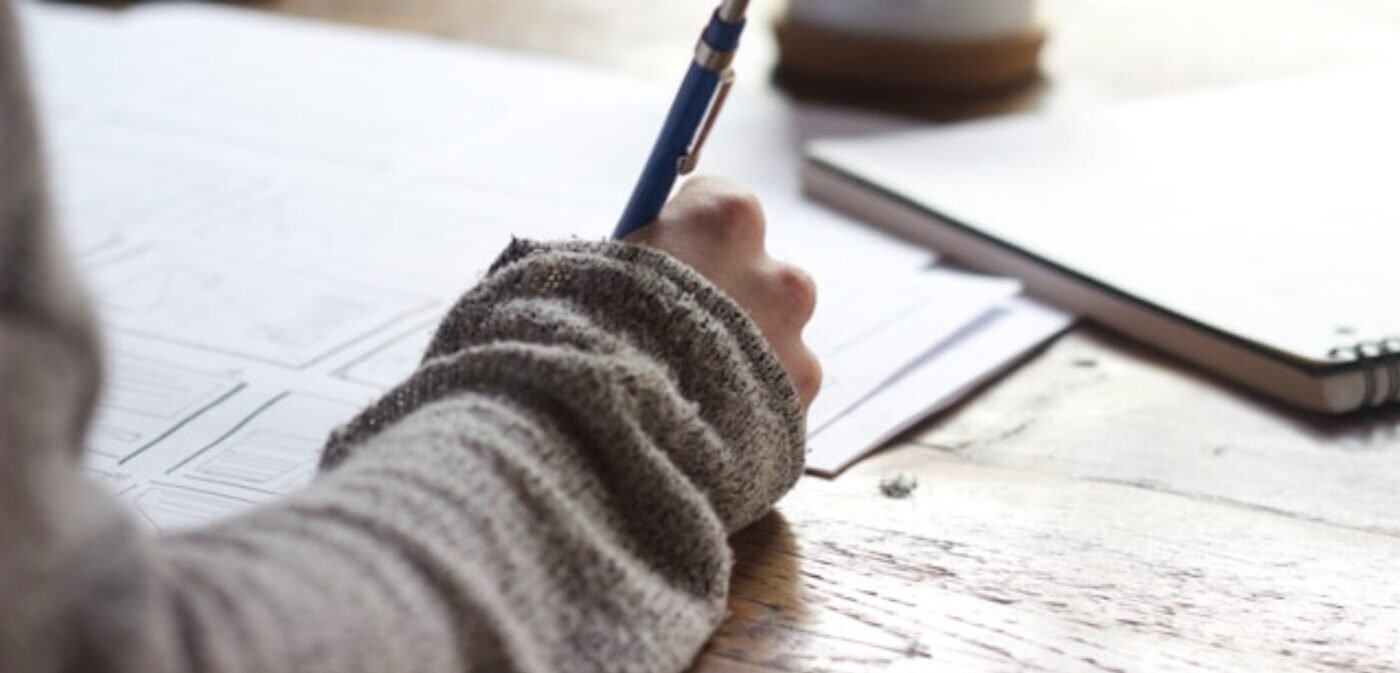 Homme assis à un bureau en bois, rédigeant des articles de blog généalogiques captivants à la main