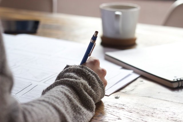 Homme assis à un bureau en bois, rédigeant des articles de blog généalogiques captivants à la main